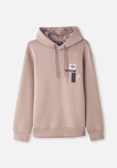 Luegenser i beige, med en frontlomme som har logopatcher. Designet med en avslappet passform og ribbekantede cuffs og nederkant. Jevn tekstur.