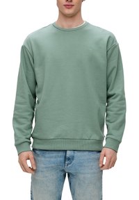 Felpa verde chiaro in un tessuto morbido e testurizzato. Collo rotondo, polsini e orlo a coste. Piccolo logo sul petto, abbinata a jeans in denim blu.