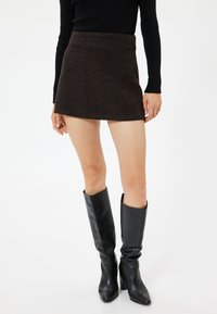 Bruine textuur mini rok gecombineerd met kniehoge zwarte leren laarzen. De rok heeft een getailleerde vorm en een subtiel patroon.