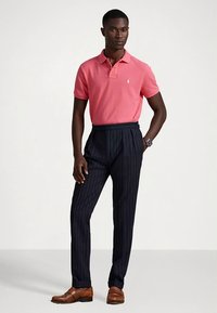 Ροζ πόλο μπλούζα με μικρό λογότυπο· μπλε σκούρες ριγέ παντελόνια· καφέ δερμάτινα παπούτσια· ομαλό ύφασμα· εφαρμοστό σχέδιο, ραμμένη εμφάνιση.