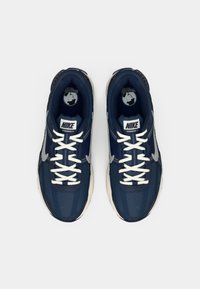 Tamsiai mėlyni Nike Vomero 5 sportbačiai turi tinklinį viršų, baltus raiščius ir pilkas detales. Padas yra šviesios spalvos su tekstūriniais akcentais.