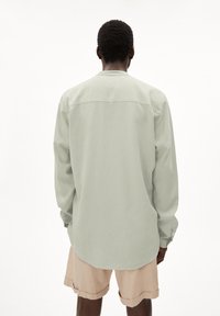 Lichtgroen langarmshirt met een eenvoudig ontwerp, zachte textuur en knoopmanchetten, gecombineerd met beige shorts. Achteraanzicht weergegeven.