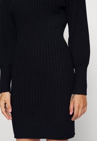 Abito a maglia ribbed nero con maniche lunghe, vestibilità slim e scollatura rotonda. Presenta un tessuto текстurizzato e un'orlo all'altezza del ginocchio.