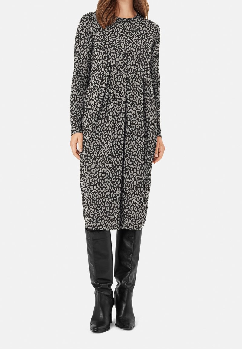 Robe à manches longues imprimé léopard gris avec un design plissé, associée à des bottes noires hautes jusqu'aux genoux pour une tenue complète.