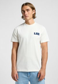 Hvid bomulds t-shirt med korte ærmer, rund halsudskæring og navy "LEE" logo på venstre bryst. Båret med lyseblå denim jeans.
