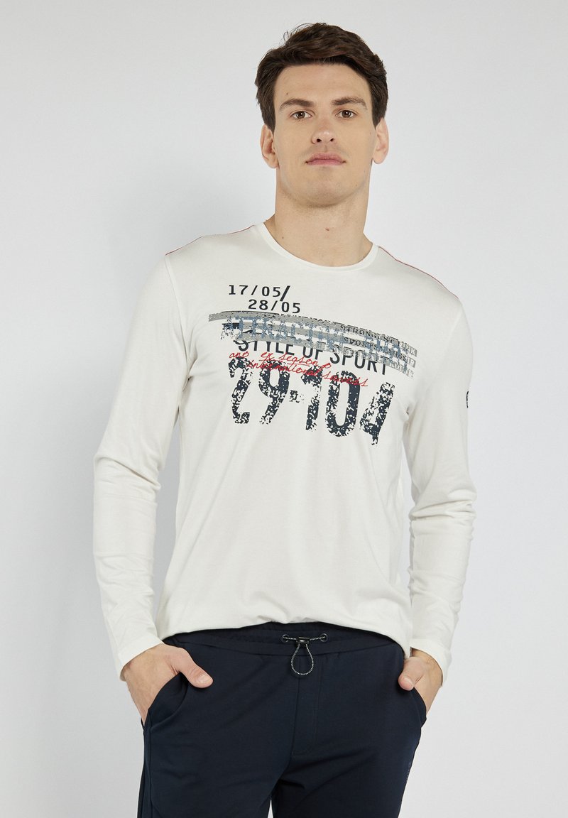 T-shirt z długim rękawem w kolorze kremowym, z graficznym wzorem tekstu w kolorze czarnym, czerwonym i szarym. Posiada okrągły dekolt i kontrastowe szwy.