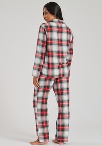 Red and black plaid pajama set in soft fabric. Features long sleeves, relaxed fit, and straight-leg pants with an elastic waistband.