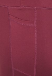 Burgunderfargede tights med en kroppsnær design, som har en sidelomme og synlige sømdetaljer, laget av mykt, elastisk materiale.