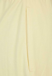 Tissu jaune clair au toucher lisse, avec une ouverture de poche latérale et un détail de surpiqûre contrastante.