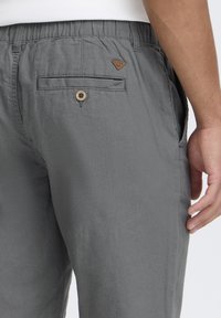 Pantalons en mélange de coton gris avec une taille élastique, comprenant une poche arrière avec une fermeture à bouton et un patch en cuir.