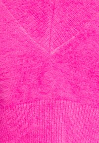 Flauschiger pinkfarbener Strickstoff mit strukturiertem Finish. Verfügt über ein V-förmiges Design und einen gerippten Saum, der eine gleichmäßige, lebendige Farbe zeigt.