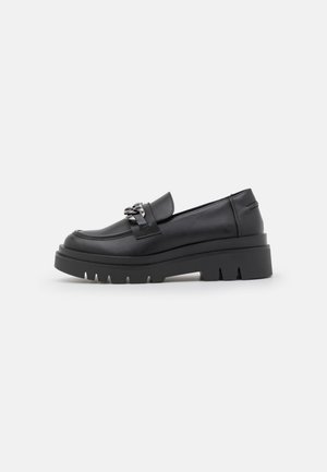Mocassins en cuir noir avec une semelle plateforme épaisse, ornés d'un accent de chaîne métallique décorative sur le cou-de-pied et d'un détail texturé sur la semelle.