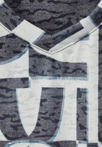 Centrer T-shirt i bomuld med et marineblåt og hvidt abstrakt mønster og V-udskæring. Dristig grafisk tekstdesign i lyseblå farve ligger ovenpå stoffet.