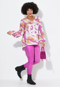 Top rosa con un patrón y un símbolo de paz blanco, combinado con leggings rosa brillantes y botas de tobillo negras con adornos. Lleva una pequeña bolsa rosa brillante.