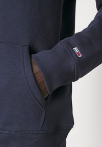 Sudadera azul marino de algodón suave, con puños de canalé y un bolsillo delantero. Incluye un pequeño detalle del logo bordado en la manga.