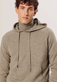 Hellbrauner Hoodies mit hohem Kragen, Kordelzügen und weicher Textur. Verfügt über Raglanärmel und ein minimalistisches Design ohne sichtbare Logos.