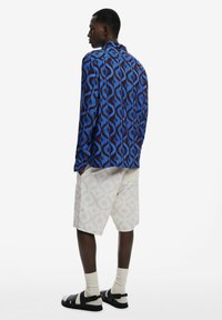 Blue and brown patterned shirt with swirled motifs, white shorts with a subtle design, and black sandals with straps.