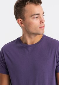 Lilla T-shirt med rund hals, lavet af blødt stof, med korte ærmer og en struktureret overflade. Enkel design uden yderligere mønstre eller accenter.