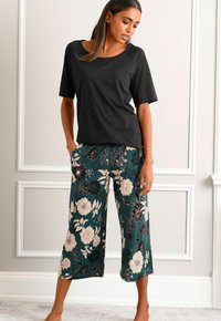 Black short-sleeve top paired with teal floral printed cropped pants featuring large white and dark flowers, smooth fabric, and relaxed fit.