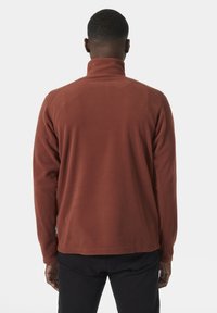 Rdzawoczerwony polarowy polar z wysokim kołnierzem; cechuje się długimi rękawami i prostym wykończeniem. Miękka tekstura z minimalnym brandingiem.