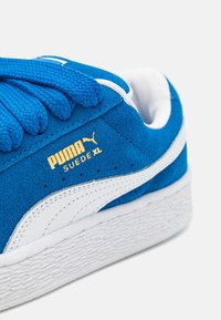 Zapatillas Puma Suede XL de un vibrante azul con parte superior de ante texturizado, acentos de cuero blanco y suela de goma blanca texturizada. Detalle de marca en dorado.