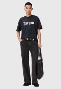 Czarna koszulka z białym napisem "Drum", w zestawieniu z czarnymi spodniami o szerokich nogawkach. Dodatki to czarny pasek i torebka z teksturowanego materiału.