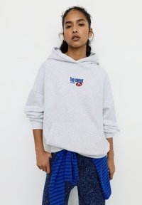 Felpa grigia con la scritta "Too sweet" in blu e rosso. Abbinata a un tessuto a righe blu annodato in vita, con leggings blu navy maculati.