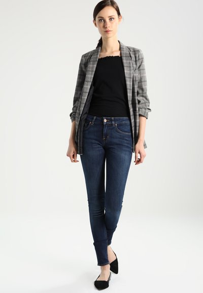 Grijze geruite blazer over een zwarte getailleerde top, gecombineerd met donkerblauwe skinny jeans en zwarte flats. Soepele stof met gestructureerd tailorwerk.