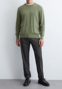 Lichtgroene gebreide trui met een ronde hals, gecombineerd met donkergrijze broek en zwarte veterschoenen. Glad textuur, slim-fit ontwerp.