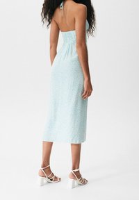 Vestido midi floral en azul claro con un cuerpo ajustado y una falda fluida. Combinado con sandalias blancas de tiras con tacones anchos.