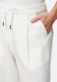 White linen pants with a drawstring waist, pleats at the front, and side pockets. Soft texture with a slightly relaxed fit.