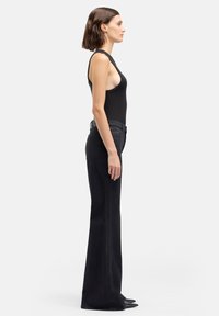 Zwart bodysuit gecombineerd met zwart, hooggetailleerde jeans met wijde pijpen. Soepele textuur en nauwsluitend ontwerp, met klassieke vijfzakkenstijl.