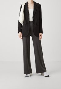Black pinstriped blazer with two buttons, white ribbed top, and gray ribbed wide-leg trousers. White sneakers complete the outfit.