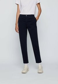 Mörkblå chinos i bomull, med rak bendesign och synlig knappstängning samt sidofickor. Bärs med en vit T-shirt.