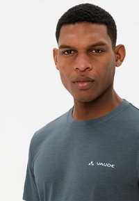 Grijze katoenen T-shirt met ronde hals, voorzien van een klein wit "VAUDE" logo aan de linkerkant, met een gladde textuur en korte mouwen.