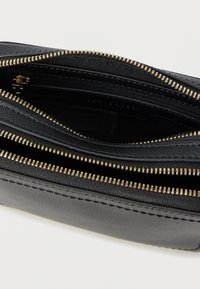 Μαύρο πορτοφόλι από δέρμα με φερμουάρ, διαθέτει πολλαπλές θήκες, φερμουάρ σε χρυσό τόνο, υφή επιφάνειας και ραφές στα άκρα.