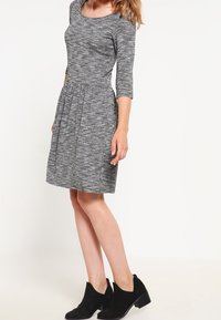 Szara, teksturowana sukienka z okrągłym dekoltem, rękawami do łokcia i rozkloszowanym dołem. Noszona z czarnymi botkami za kostkę.