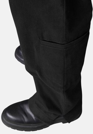 Schwarze Baumwollhose mit einer Seitentasche, kombiniert mit schwarzen Lederstiefeln, aus einer niedrigeren Perspektive aufgenommen, die den Saum und die Textur betont.