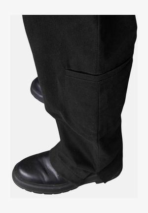 Schwarze Baumwollhose mit einer Seitentasche, kombiniert mit schwarzen Lederstiefeln, aus einer niedrigeren Perspektive aufgenommen, die den Saum und die Textur betont.