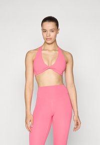Top desportivo rosa com um design de halter e frente torcida, combinado com leggings rosa de cintura alta. Tecido suave e elástico sem padrões visíveis.