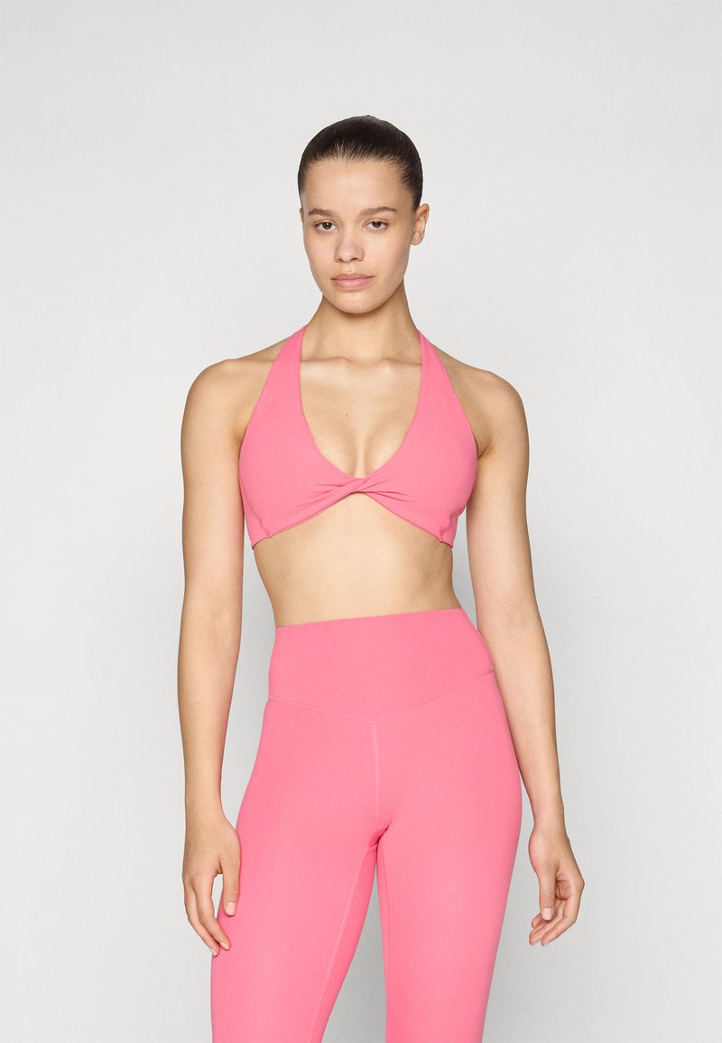 Top desportivo rosa com um design de halter e frente torcida, combinado com leggings rosa de cintura alta. Tecido suave e elástico sem padrões visíveis.