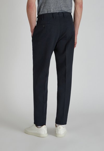 Pantaloni blu navy con una texture liscia, taglio slim, passanti per cintura, tasche posteriori con bottoni, abbinati a sneakers bianche.