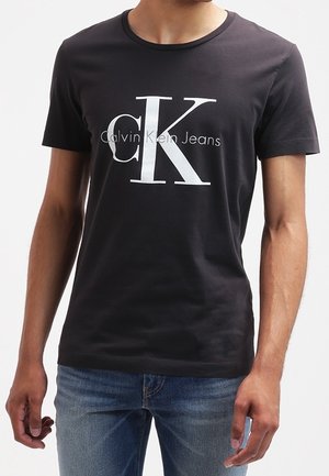 T-shirt nera in cotone con collo rotondo, caratterizzata da un grande logo "CK" bianco e il testo "Calvin Klein Jeans" sottostante in un design minimalista.