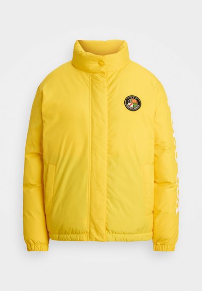 Geel pufferjack met een hoge kraag, twee zijzakken en geribbelde manchetten. Heeft een cirkelvormig logo op de borst en tekst langs de mouw.