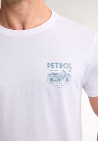 Bílý bavlněný tričko s motivem světle modré grafiky motocyklu a textem "PETROL REG.5026 U.S.A. OUTDOOR SUPPLY FLORIDA."