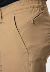 Pantalones ligeros color beige con una tela texturizada, cinturilla elástica y un bolsillo lateral con cremallera para mayor funcionalidad.