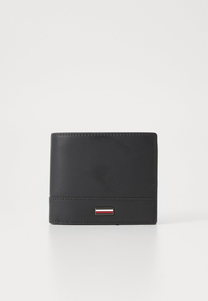 Portefeuille en cuir noir avec une texture lisse, de forme rectangulaire, des coutures visibles et un petit logo en métal avec des accents rouges et argentés.
