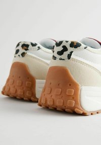Sneakers z beżowym zamszem i białą tekstylną cholewką, z leopardzim akcentem na pięcie oraz teksturowaną, pomarańczową gumową podeszwą.