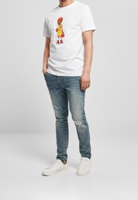 Witte katoenen T-shirt met een kleurrijk cartoonfiguurtje. Draagt het met versleten blauwe spijkerbroeken en witte sneakers. Casual pasvorm en ontwerp.