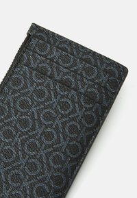 Tarjetero negro con patrón de logo en relieve, que cuenta con compartimentos horizontales para tarjetas y un acabado texturizado. Los bordes cosidos aportan durabilidad.